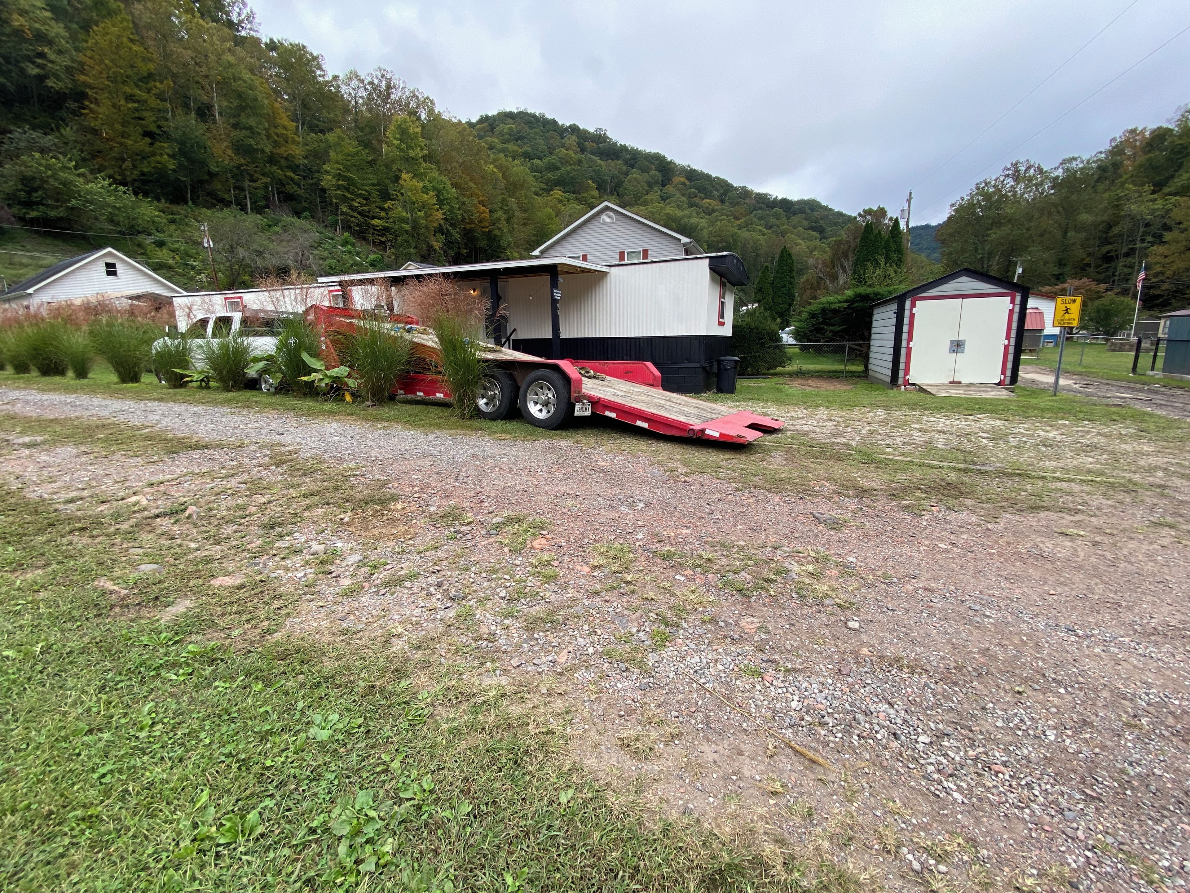 A gravel driveway leading to a house with a covered porch and a trailer parked nearby.
