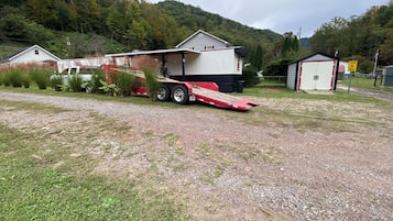 A gravel driveway leading to a house with a covered porch and a trailer parked nearby.
