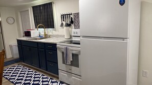 Cocina compacta con refrigerador, microondas, pileta y un juego de cuchillos en la pared.