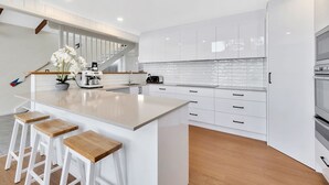 Une cuisine moderne avec des meubles blancs, un grand îlot central doté de tabourets, un four encastré et une machine à café.