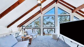 Une pièce spacieuse avec un plafond en pente, de grandes fenêtres, un téléviseur à écran plat, un canapé, une petite table et un télescope.