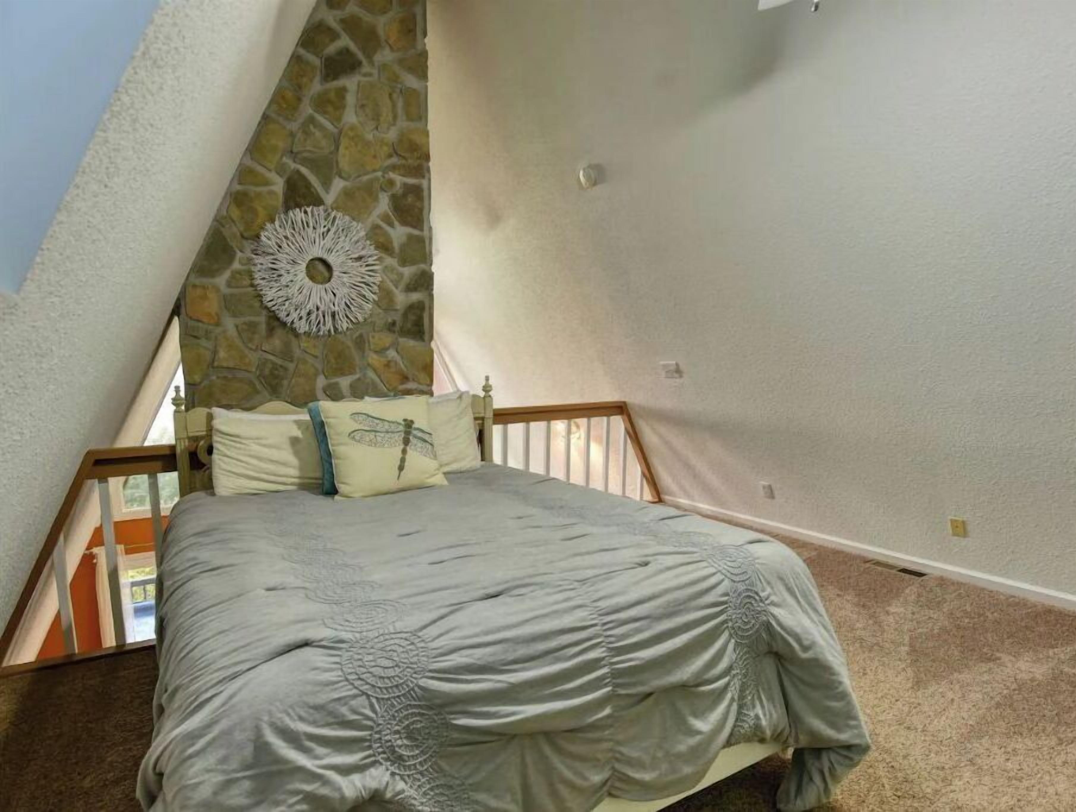 Un dormitorio con una pared de piedra decorativa, un tapiz ornamental y una cama con cubrecama gris.