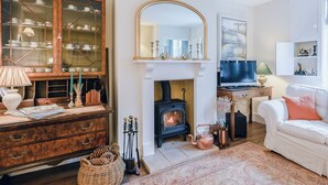 A cozy living room with a fireplace, a television, a white sofa, and a wooden cabinet with glass doors. - 3 bedroom accommodation in Holt (Holt)