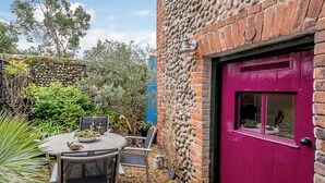A patio with a table and chairs, a purple door, and a stone wall. - 3 bedroom accommodation in Holt (Holt)