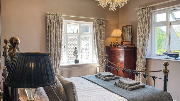 A bedroom with a bed, a chandelier, a dresser, and a window with curtains. - 3 bedroom accommodation in Holt (Holt)