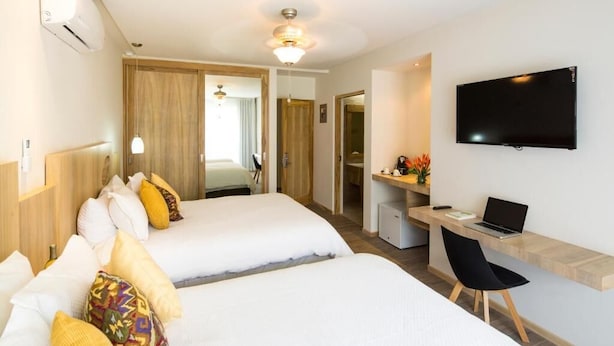 Una habitación de hotel con dos camas, un escritorio con una computadora portátil, un televisor y un ventilador de techo.