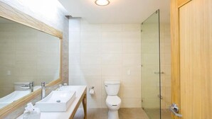 Un baño con un espejo grande, dos lavamanos, un inodoro y una ducha con cerramiento de vidrio.