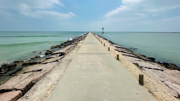 A concrete pier extending into calm waters with a clear sky above. - Cute, Cozy and Clean cottage by the Sea! (Freeport)