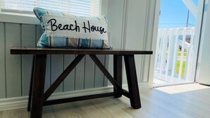 A wooden table with a cushion labeled "Beach House" in a room with a view of a balcony. - Cute, Cozy and Clean cottage by the Sea! (Freeport)