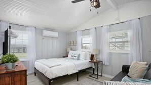 A bedroom with a bed, bedside tables, a desk, a chair, and a ceiling fan. - Cute, Cozy and Clean cottage by the Sea! (Freeport)