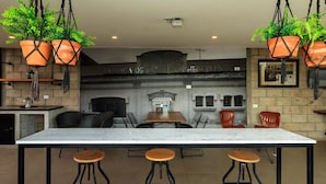 Un espace bar doté d’un comptoir en marbre, de tabourets en métal noir et de jardinières en terre cuite suspendues.