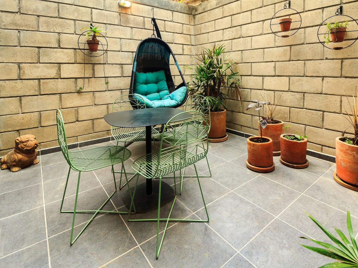 Un patio con una silla colgante, una mesa redonda y varias plantas en macetas.
