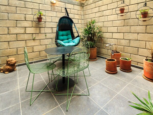 A patio area with a hanging chair, a round table, and several potted plants.