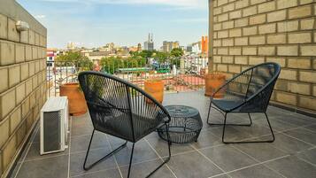 Una terraza en la azotea con dos sillas de malla metálica negra y una pequeña mesa redonda, una planta en maceta y un radiador.