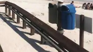 Une plage avec une promenade en bois, une poubelle et un ciel dégagé.