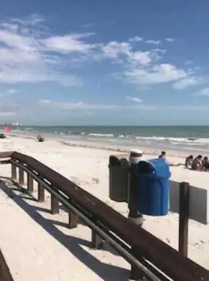 A beach with a wooden walkway, trash bins, and a clear sky.