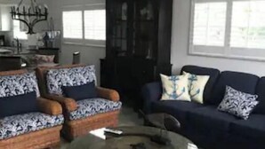 A living room with a dark-colored sofa, a patterned armchair, and a round coffee table. There is a dark wooden cabinet and a ceiling fan. - Beach Property with get away feeling. (Fort Myers Beach)