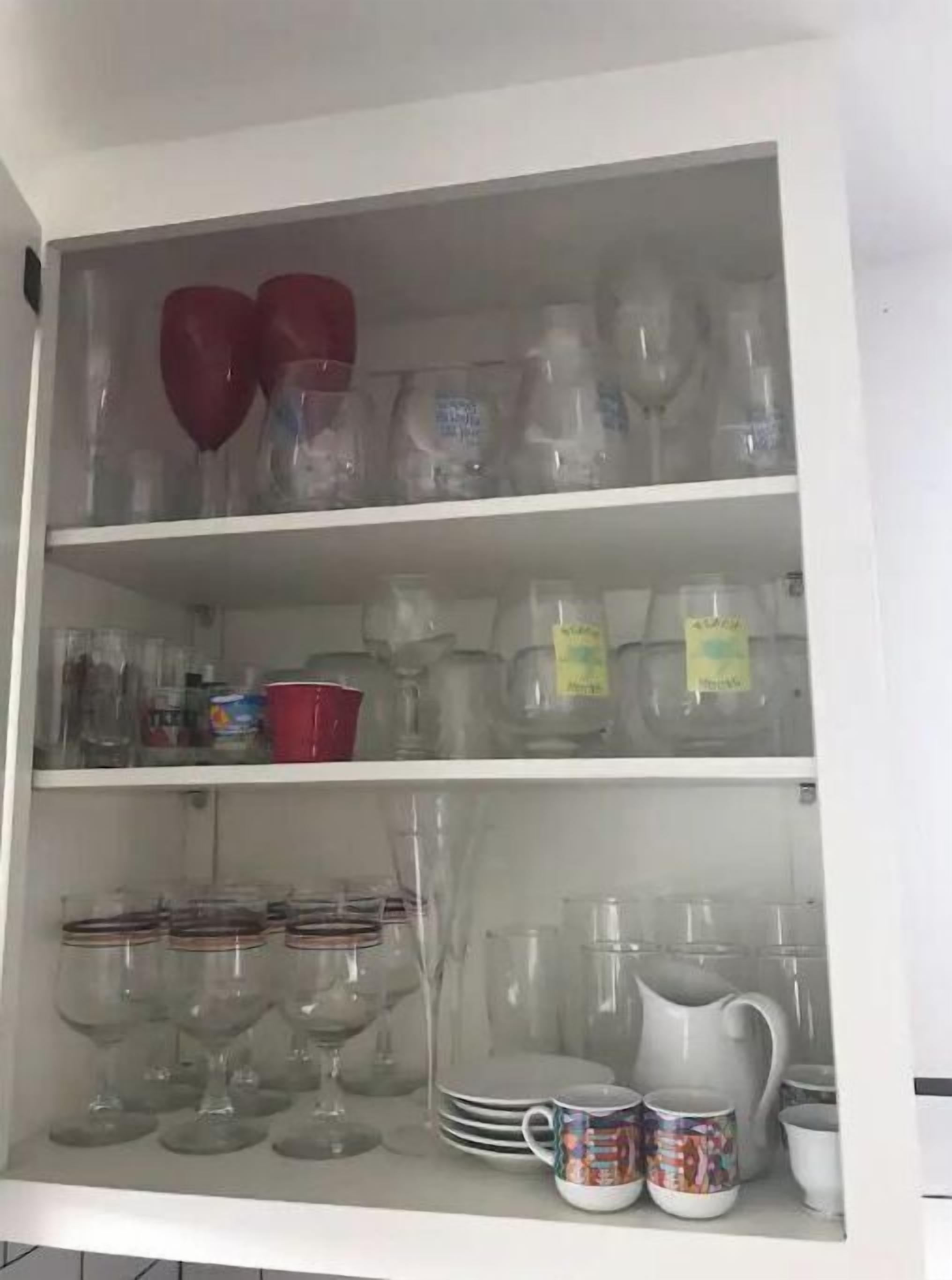 Un meuble de cuisine doté d’étagères où sont rangés divers objets en verre, notamment des verres à vin, des verres à cocktail et un pichet décoratif.