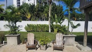 A patio with two wooden Adirondack chairs and a small table, surrounded by potted plants and a neatly trimmed hedge. - Beach Property with get away feeling. (Fort Myers Beach)