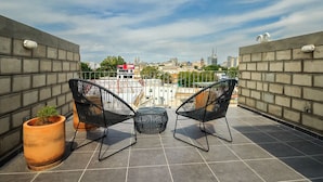 Una terraza en la azotea con dos sillas negras, una mesa redonda y una maceta de terracota grande con una planta.