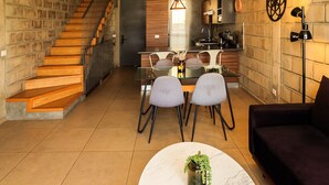 Una cocina moderna con una isla central, un comedor con mesa y sillas de vidrio, y una escalera que sube a otro nivel.