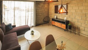 Una sala de estar moderna con sofá, mesa de comedor, sillas, una pequeña cocina y un ventanal grande.