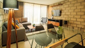 A modern living room with a sofa, a glass dining table, and a TV mounted on a brick wall. - Inspiring Loft w/Gym & Coworking | 2 BD | Tribu Colón (Guadalajara)
