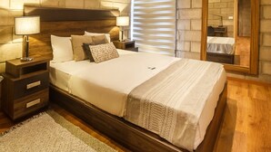 A bedroom with a wooden headboard, a large bed with white bedding, a nightstand with a lamp, a mirror, and artwork on the wall. - Inspiring Loft w/Gym & Coworking | 2 BD | Tribu Colón (Guadalajara)