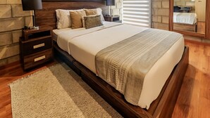 Ein Schlafzimmer mit einem großen Bett, einem Holz-Kopfteil, zwei Nachttischen mit Lampen, einem gewebten Teppich und einer Ziegelwand.