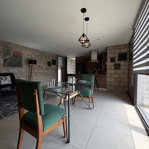 Un espace de salle à manger moderne avec une table en verre, des chaises à revêtement vert et un luminaire suspendu.