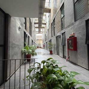A narrow corridor with tiled flooring, potted plants, and a red fire alarm box. - Elegant Solo Loft + Open Air | 1 BD | Tribu Colón (Guadalajara)