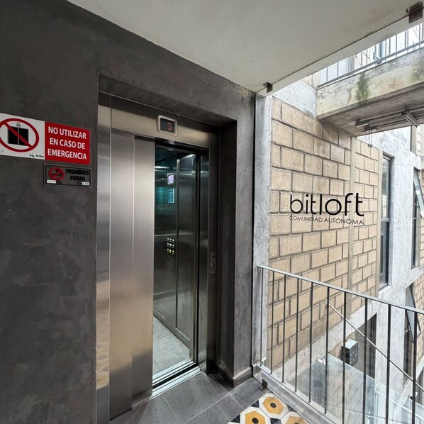 Un ascenseur doté d’un écran numérique, d’un panneau « interdiction de fumer » et d’une façade d’immeuble sur laquelle on peut lire l’inscription « bitloft ».