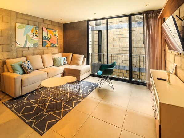 A modern living room with a sofa, coffee table, and a view of a brick building through large windows.
