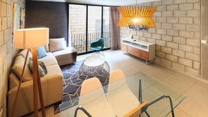 Una sala de estar moderna con una mesa de comedor de vidrio, un sofá, una silla, una lámpara y un elemento decorativo de iluminación.