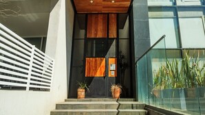 A modern building entrance with a wooden door, a glass railing, and potted plants.