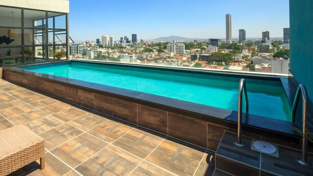 A rooftop swimming pool with a city view, a glass-enclosed area, and a tiled deck.