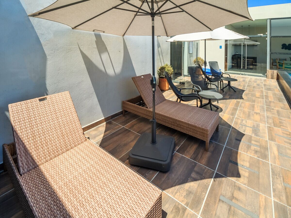 Une terrasse sur le toit, avec des fauteuils de salon en osier, une table et un parasol.