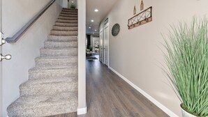 Un couloir avec un escalier recouvert de moquette, une plante en pot et une horloge fixée au mur.