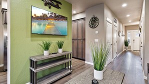 Un couloir moderne avec un téléviseur fixé sur un mur vert, un plancher en bois et des plantes en pot.