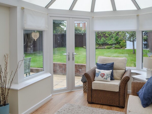 A conservatory with a wicker sofa, a small table, and a view of a garden.