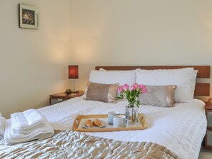 A neatly made bed with pillows, a tray with croissants and mugs, and a vase with flowers.