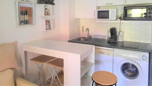 Une cuisine compacte équipée d’un four à micro-ondes, d’une machine à café et d’un lave-linge. Un petit coin repas avec une table et des chaises est également à disposition.