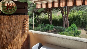 Un balcon donnant sur un jardin, une clôture en bambou et une enseigne pour le whisky JB Scotch.