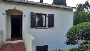 Un bâtiment à l’extérieur blanc, avec des portes numérotées et une petite fenêtre dotée de volets.
