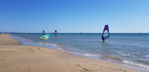 Ein Strand mit Windsurfern und Menschen, die am Ufer entlanggehen.