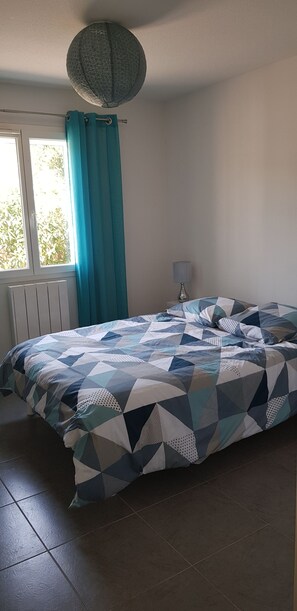 Ein Schlafzimmer mit Bett, Fenster mit Vorhängen, Lampe und Heizkörper.