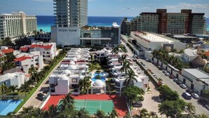 Un complex turístic amb diversos edificis, incloent un hotel alt, una zona de piscines i una pista de tennis.