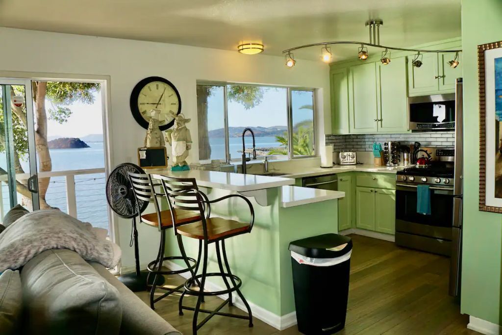 Una cocina con vista al agua, armarios verdes, una estufa y un ventilador.
