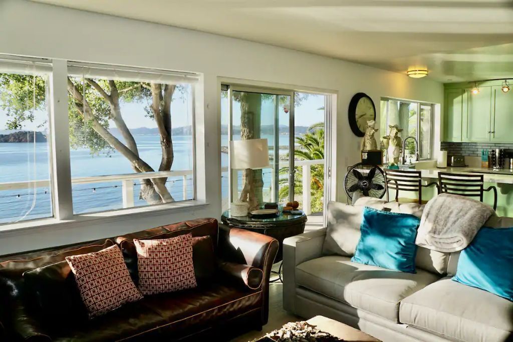Una sala de estar con vista al mar, un comedor y una cocina con armarios verdes.