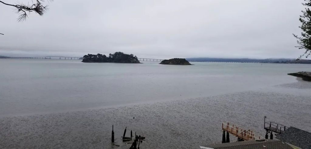 A beach with a wooden pier and a bridge in the background.